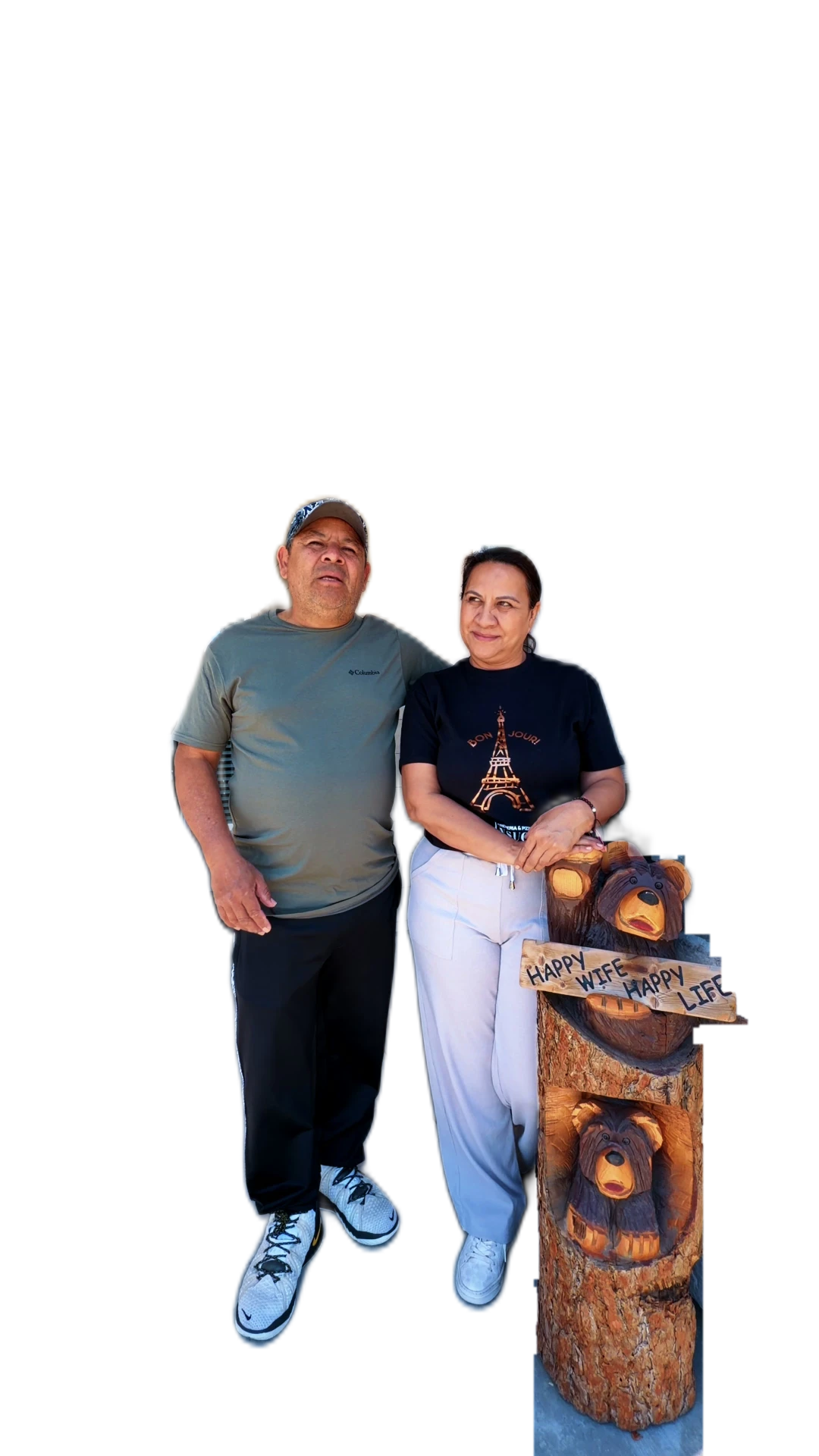 Una pareja en el porche de su casa nueva, junto a un oso tallado que dice Happy Wife Happy Life